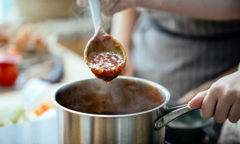 Panela pequena com calda escura de frutas vermelhas sendo mexida com colher de pau